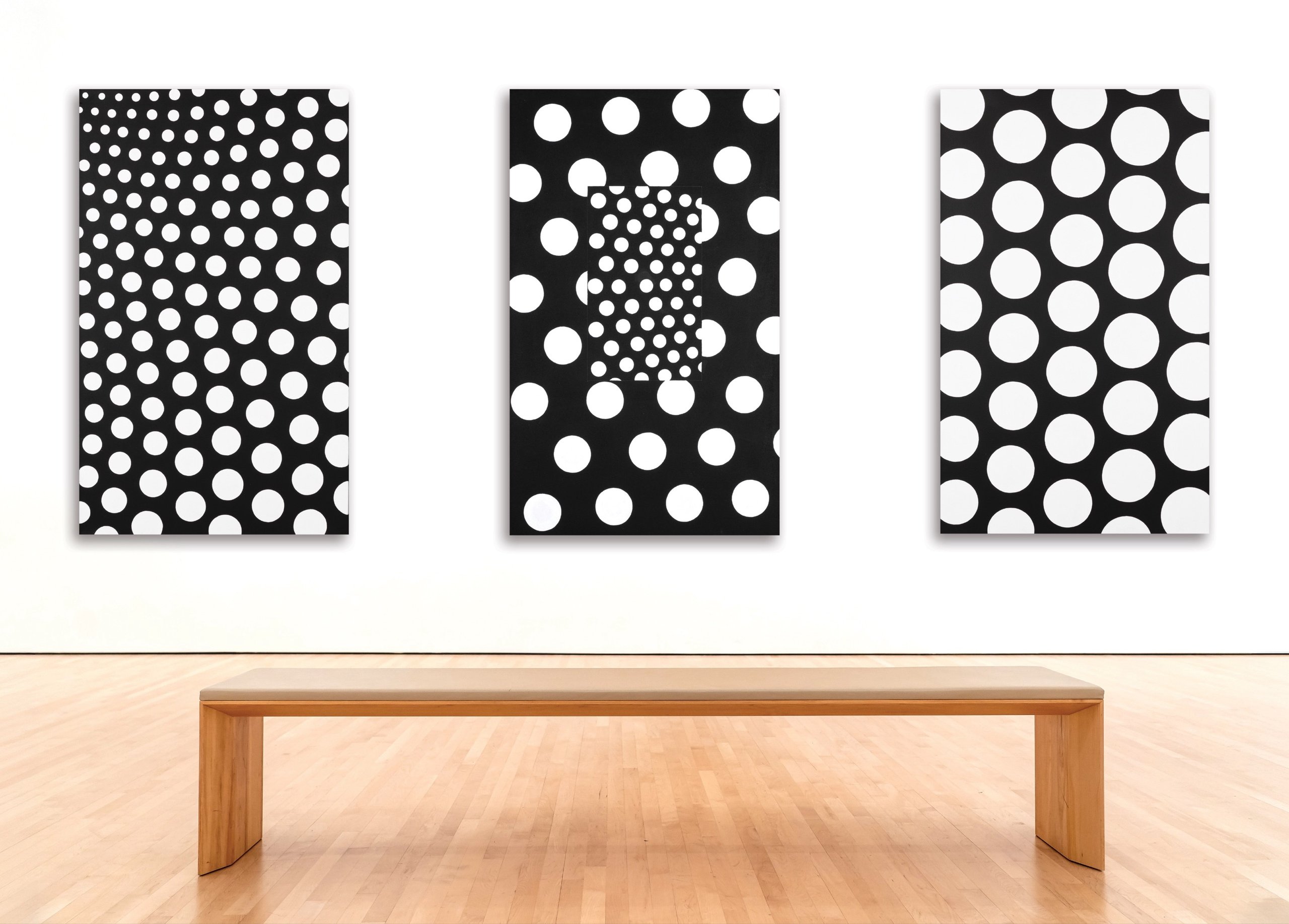 Three large black-and-white dot paintings on canvas hanging above a wooden gallery bench.